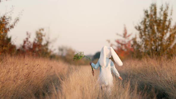 Funny Child Boy in White Bunny Costume Running From Camera on Yellow Fall Grass