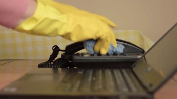 Hands in rubber gloves cleaning office phone with cloth