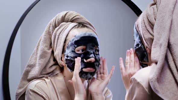 Young happy woman in towel making face mask and looking in mirror in stylish bathroom. The woman use