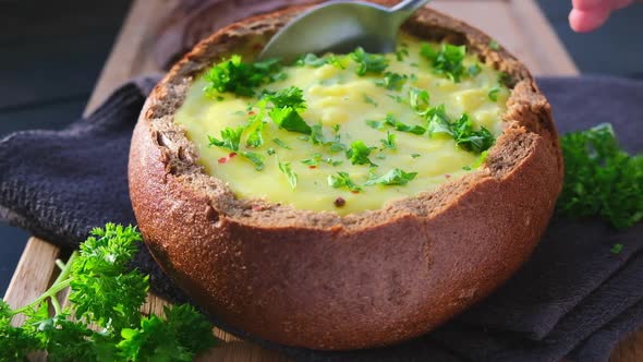 Cheese soup in a bread bowl on wooden board.