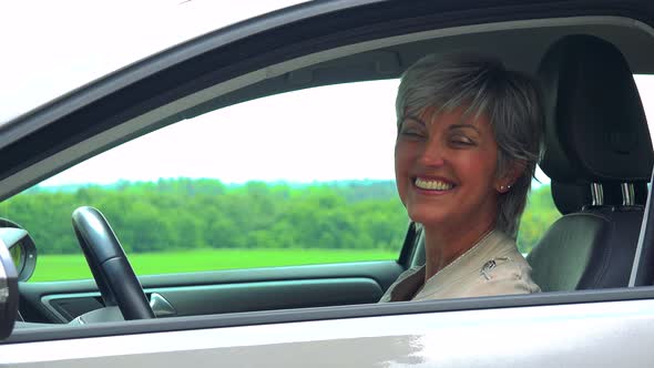 Middle Aged Woman Sits in the Car and Smiles To the Camera - Car Stands on the Verge of Road