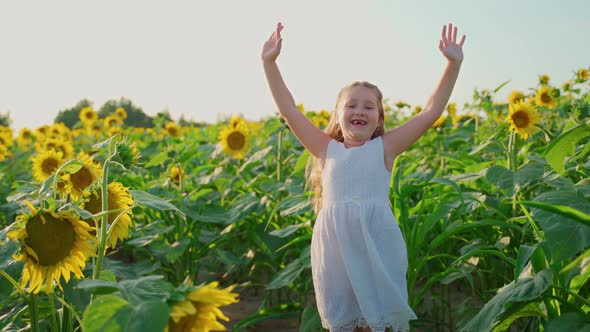 Girl jumping at sunflowers field looking at camera smiling. Bright sunny day