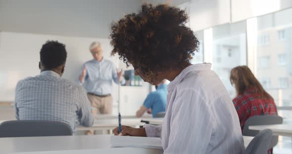 African Female College Student Sitting at Desk and Studying in Classroom Smiling at Camera