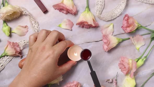 Hands pouring melted wax onto an envelope near pink flowers