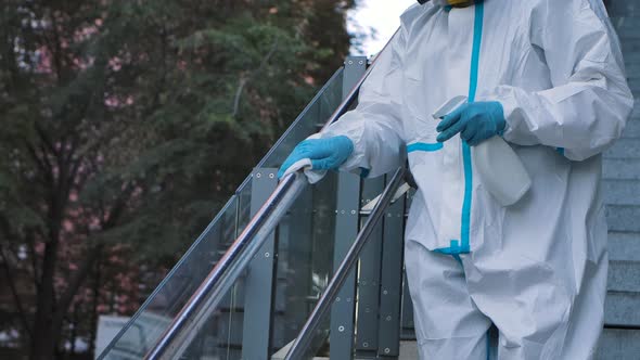 Medic in a White Protective Suit Disinfects a City Street. A Virologist in a Protective Suit