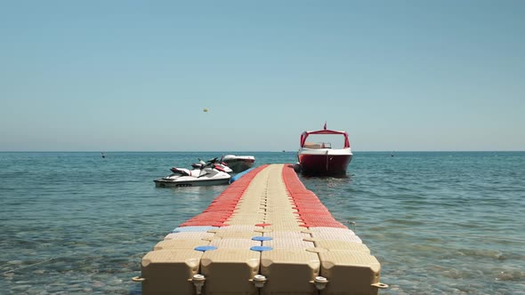 Plastic pontoon in sea with moored yacht and jet bikes.