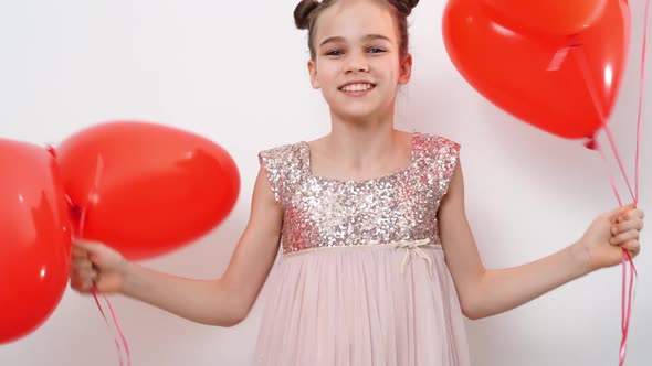 Teen Girl Dances Laughs with Red Balls of Hearts Near White Wall