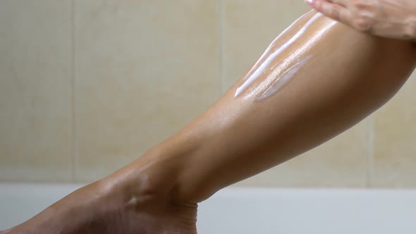 Woman Applying Lotion After Waxing Legs in Bathroom, Hair Removal and Skin Care