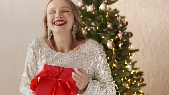 Woman shaking wrapped present gift box and listening what's inside with christmas tree