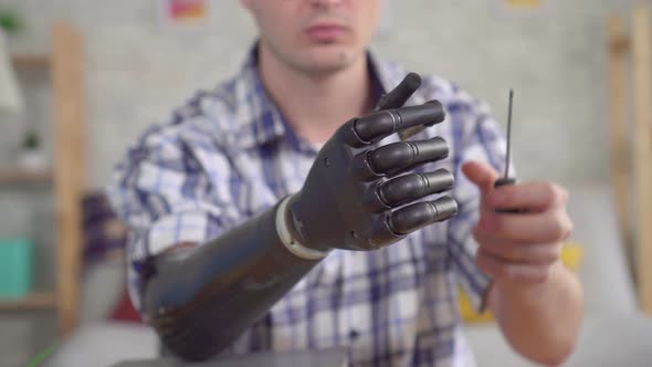 Young Man Adjusts a Bionic Prosthetic Hand with a Screwdriver Close Up