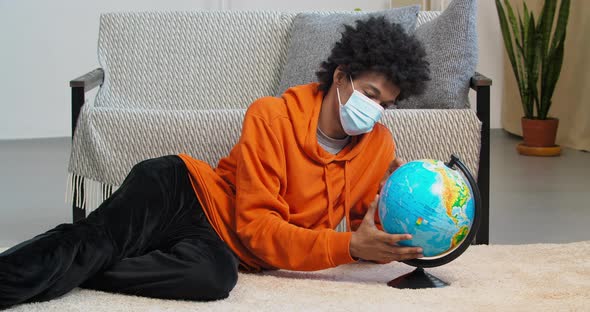 Afro American Sad Guy Man Lies on Floor in Living Room Wears Face Protective Medical Mask Longingly