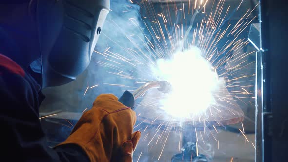 Worker welding a piece of metal. Sparks, strong light. Worker using a special helmet as a protection