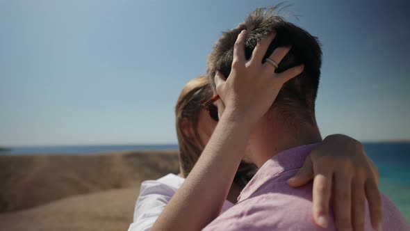 a Man in a Pink Tshirt and Sunglasses and a Woman with Long Hair in a White Shirt are Hugging on a