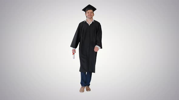 Smiling Male Student in Graduation Robe Walking with His Diploma on Gradient Background