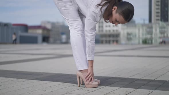 Side View Legs of Young Slim Woman in White Outfit and Beige Highheels on City Square Outdoors