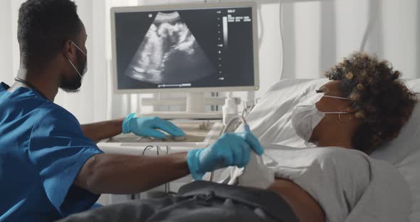 Afro Male Doctor in Medical Protective Mask Doing Ultrasound Screening for Pregnant Woman at Clinic