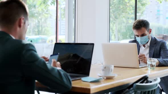 Businessmen wearing protective mask using smartphones in cafe