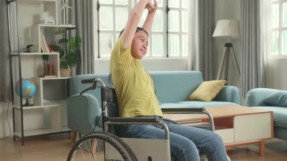 Asian Kid Girl Sitting In A Wheelchair And Stretching At Home