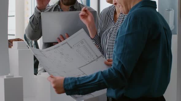 Close Up of Team of Colleagues Working on Building Model Design with Computer and Blueprints