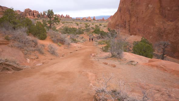 People hiking through Arches National Park towards Landscape Arch on a cloudy day, tilt
