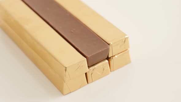 Lot of golden paper wrapped chocolate bars on white  with one opened  background slow tilt 4K 2160p 