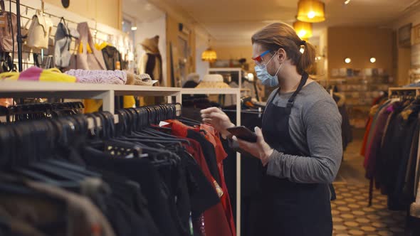 Male Shop Assistant in Safety Mask Using Digital Tablet Checking Clothes