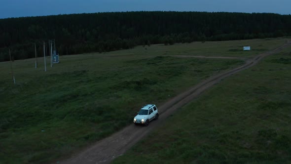 Aerial View of a Car Driving in Nature on a Field at Sunset