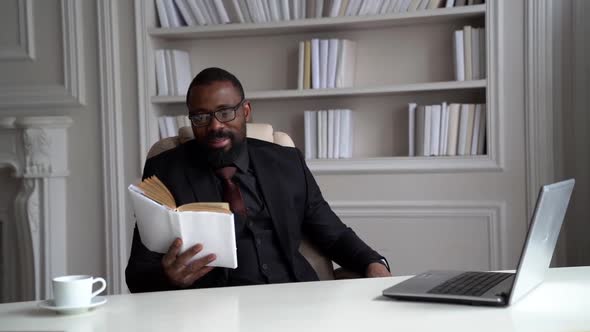 Afro-american Rich Man Is Resting in His Home Office, Reading Book Sitting in Armchair