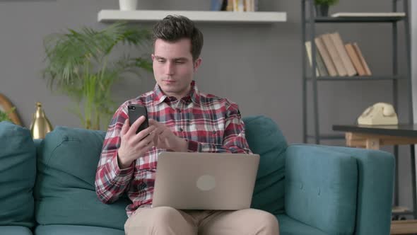 Man with Laptop Using Smartphone on Sofa