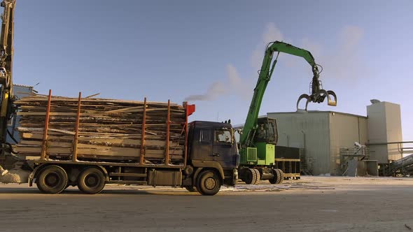 A Track Material Handler is Loading Logs Onto a Conveyor at the Factory