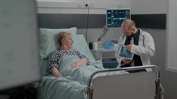 Medic Pointing at Tablet Display with Radiography for Ill Woman