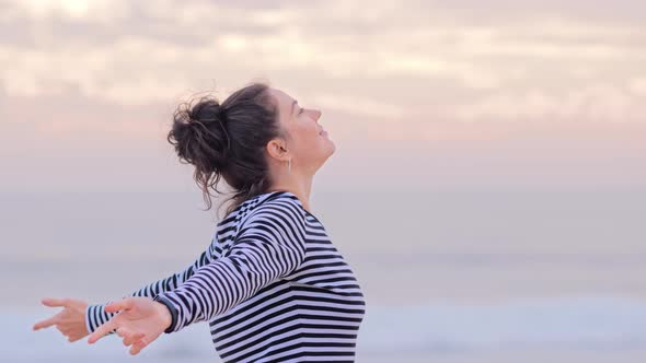 Happy Woman with Arms Up in Striped Shirt at the Beach Enjoying Sunset