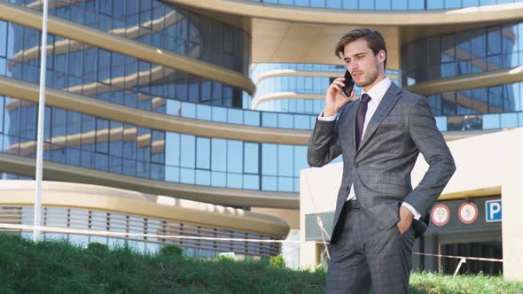 Businessman, Top Manager in a Suit Stands Near a Glass Skyscraper and Talking on a Mobile Phone