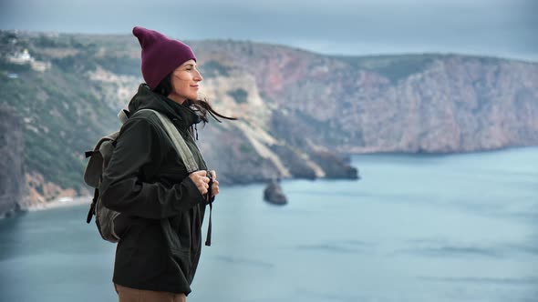 Smiling Hipster Female Tourist Admiring Nature Scenery From Mountain Peak Enjoying Trekking Vacation