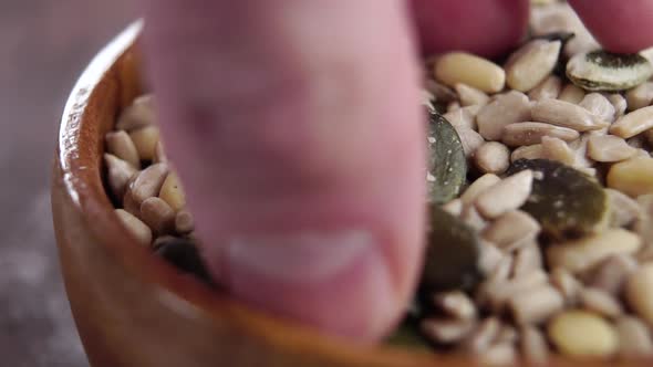 Seed mix in rustic wooden bowl. Hand takes a pinch. Falling grains in slow motion