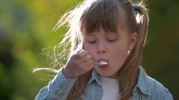 Child Girl Eating Icecream with a Spoon Outdoors