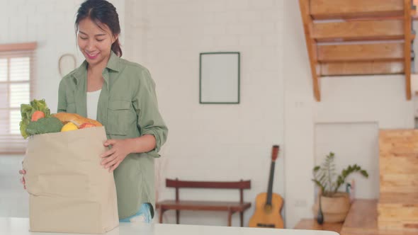 Asian women holding grocery shopping paper bags at home.