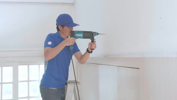 Asian Man Technician Worker On A Ladder Use Electric Drill On Wall