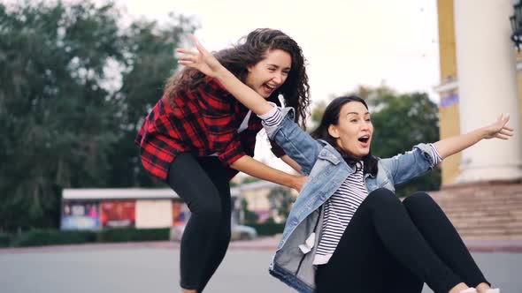 Slow Motion of Cheerful Young Women Friends Riding Skateboard Sitting on It and Pushing It in the