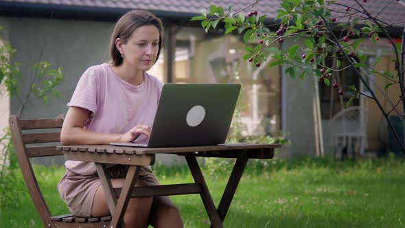 A Woman Works In Garden With Her Laptop