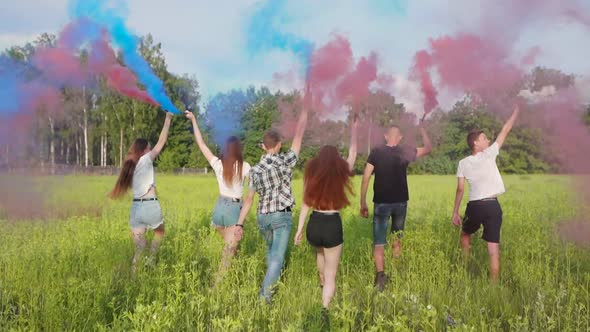Cheerful Friends Spray Colored Smoke on a Meadow in Summer.