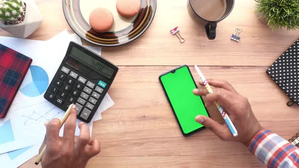 Hand Using Smart Phone and Calculator on Table  Top Down