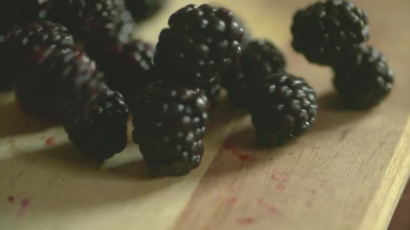 Slow motion footage of a bunch of plump, ripe blackberries dropping on to a wood cutting board