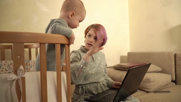 A Woman is Talking By Video Call Using Laptop and Her Son is Watching on It Standing in His Crib