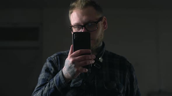 Man in Glasses Looks Carefully To His Phone in the Dark Environment, People with Gadgets, Surfing