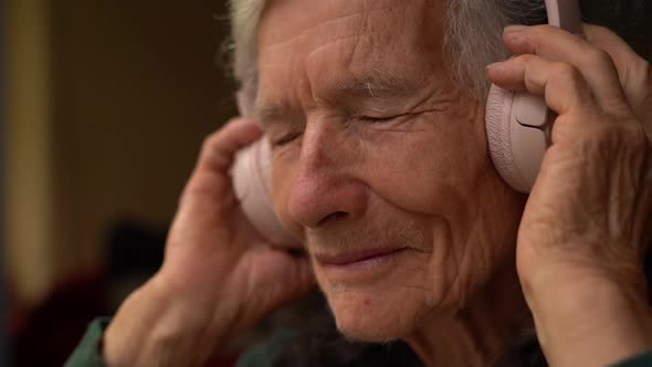 Cheerful Senior Woman Listening Music with Big Pink Wireless Headphones