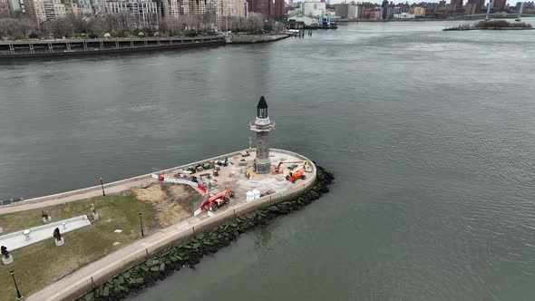 An aerial view of the Roosevelt Island lighthouse on a cloudy day. The east river is still, Manhatta