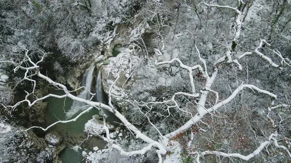 Waterfall Flowing Down From Rocks Shot Through the Branches of a Tree in Winter