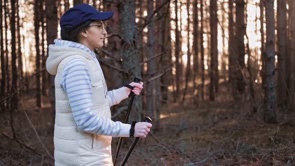 Confident Woman in Cap and Glasses Exercising Scandinavian Walk in Forest