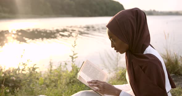 Black Woman in White Dress Reading at the River Bank